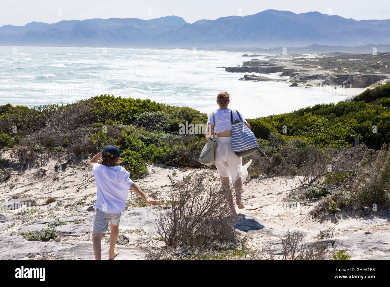 Teenager und jüngerer Bruder mit Blick auf einen Strand und eine felsige Küste mit Wellen, die an der Küste krachen. Stockfoto