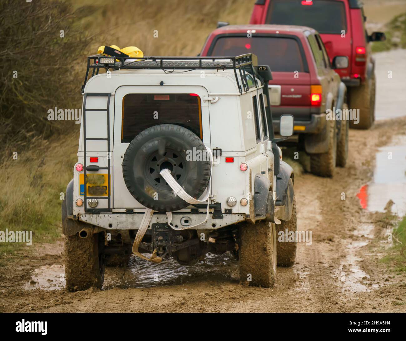 Geländewagen im Geländewagen, die über Schlamm und Wasser geloggte Gelände fahren, Salisbury Plain Wilts UK. Land Rover, Jeep Rubicon, Cherokee, Mitsubishi, Suzuki Stockfoto