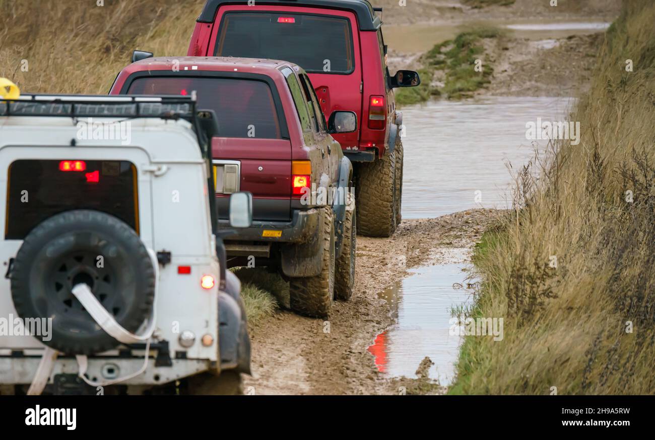 Geländewagen im Geländewagen, die über Schlamm und Wasser geloggte Gelände fahren, Salisbury Plain Wilts UK. Land Rover, Jeep Rubicon, Cherokee, Mitsubishi, Suzuki Stockfoto