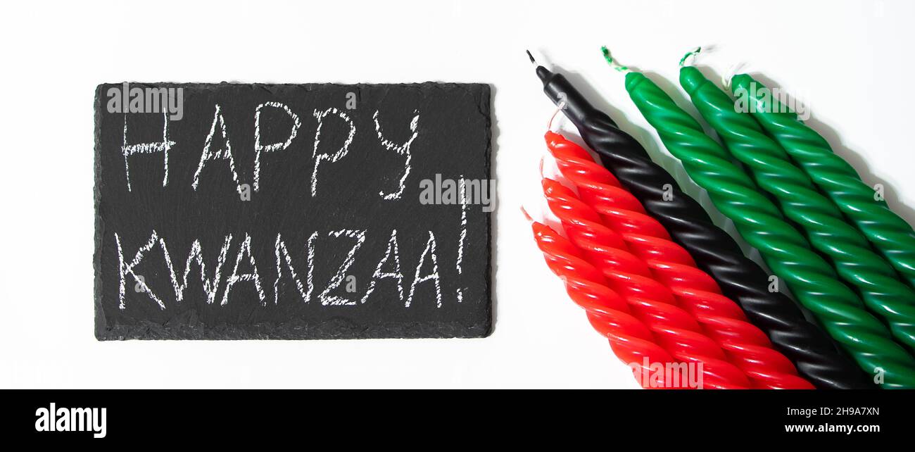 Happy Kwanzaa Konzept. Afro-amerikanischer Feiertag. Gratulationsschriftzug und sieben Kerzen - rot, schwarz und grün. Afrikanisches Erbes-Symbol auf einer weißen BA Stockfoto
