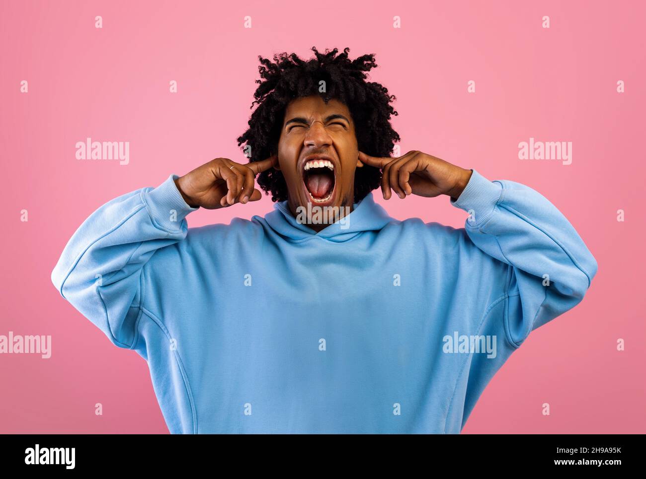 Verrückter schwarzer Teenager, der schreit, Ohren bedeckt und Augen schließt über rosa Studiohintergrund Stockfoto