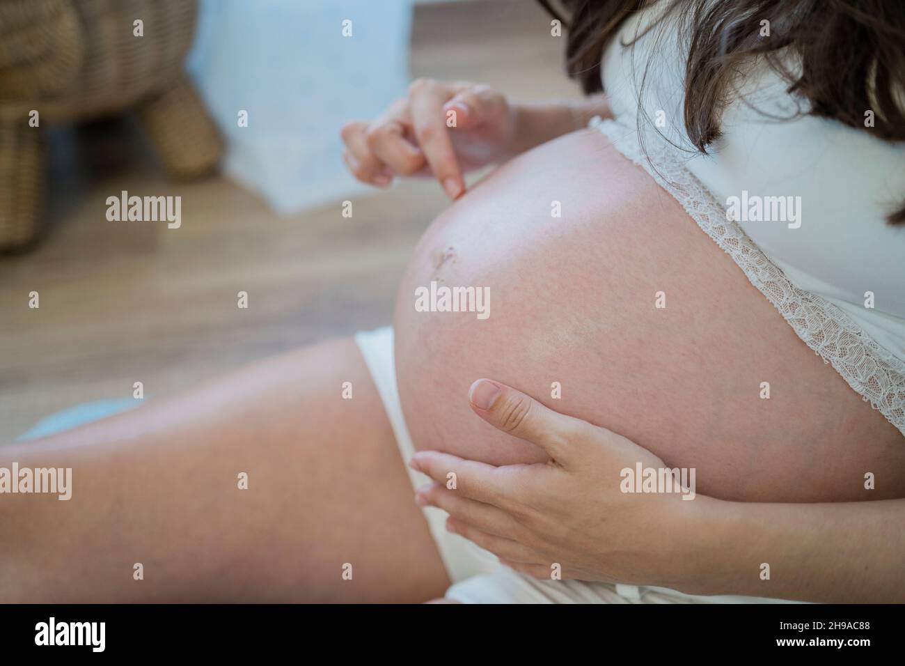 Nicht erkennbare Schwangerin, die sich auf dem Boden ruht und den Bauch sanft berührt Stockfoto