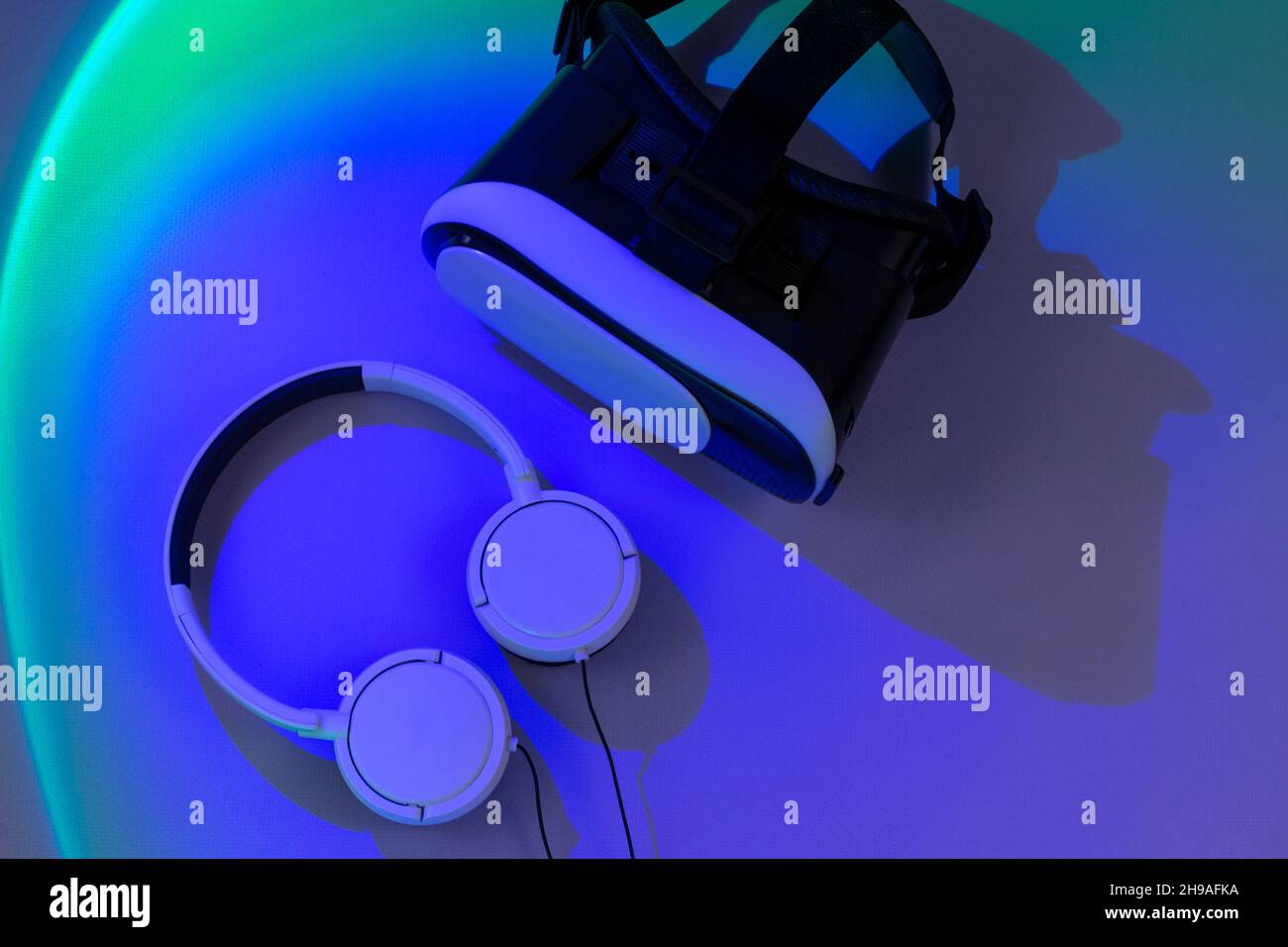 Virtual-Reality-Brille und Kopfhörer auf violettem Hintergrund mit grünen Lichtern. Set für Spiele, Cyber-Sport. Draufsicht Stockfoto