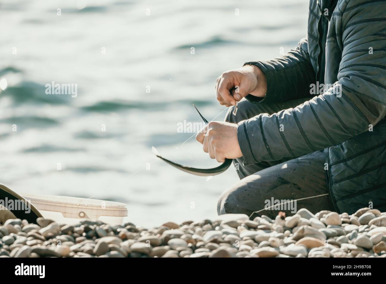 Nahaufnahme der Hände des Fischers, die den gefangenen Seegarfisch vom Haken nehmen. Mann Hobby Angeln auf dem Meer strafft eine Angelschnur Haspel Fisch Sommer. Ruhig Stockfoto