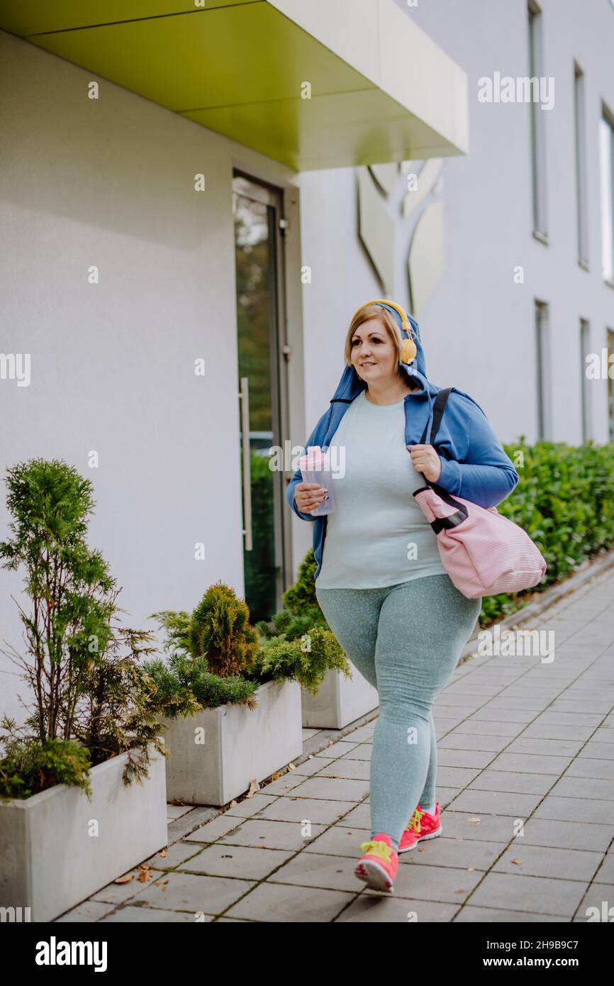 Glückliche übergewichtige Frau in Sportkleidung im Freien auf dem Weg zum Fitnesscenter Stockfoto