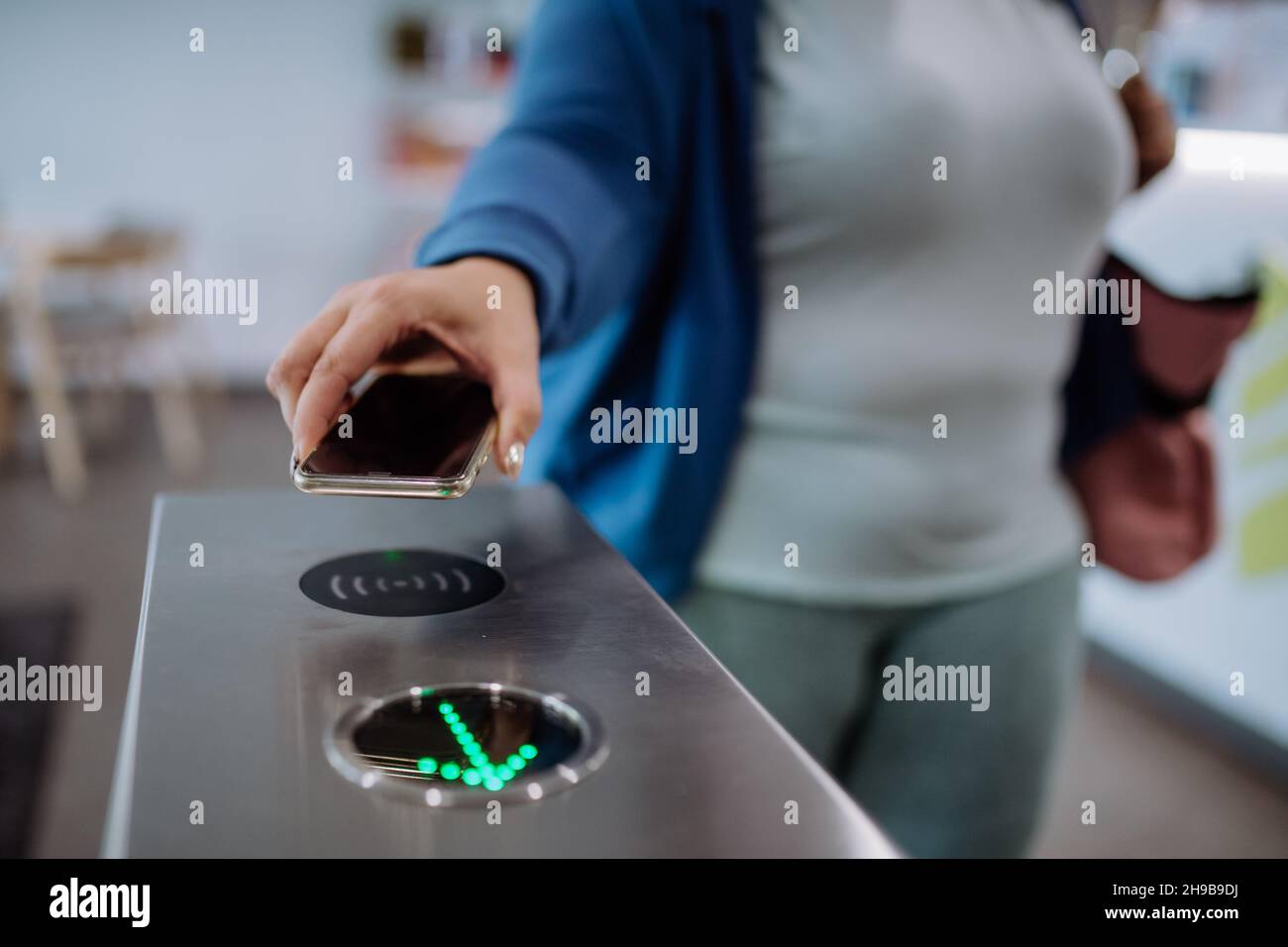 Weibliche Hand, die das Smartphone benutzt, um die automatische Tormaschine im Fitnessstudio zu öffnen Stockfoto