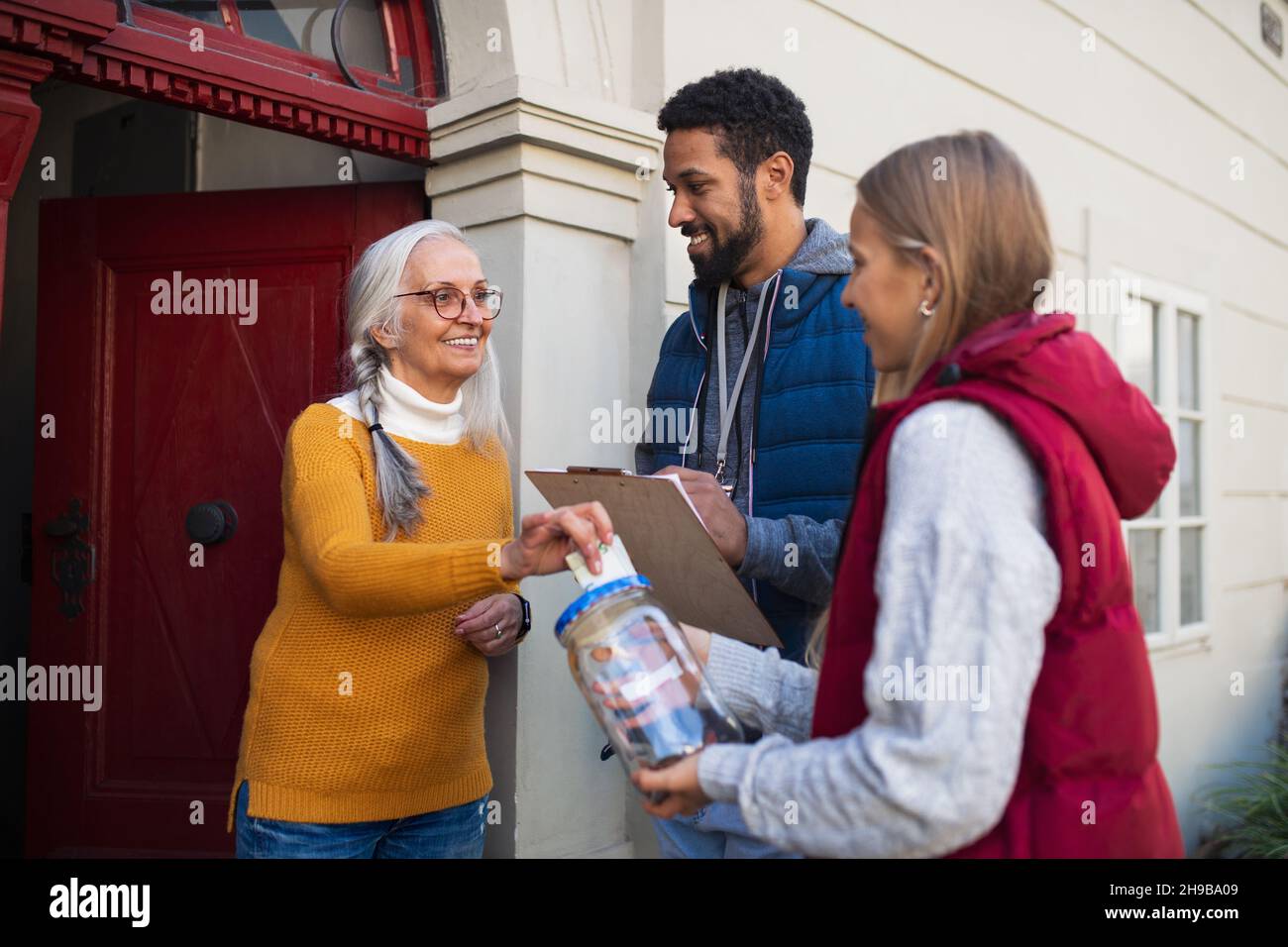 Junge Spendenaufsteller von Tür zu Tür, die mit älteren Frauen sprechen und Geld für wohltätige Zwecke auf der Straße sammeln. Stockfoto