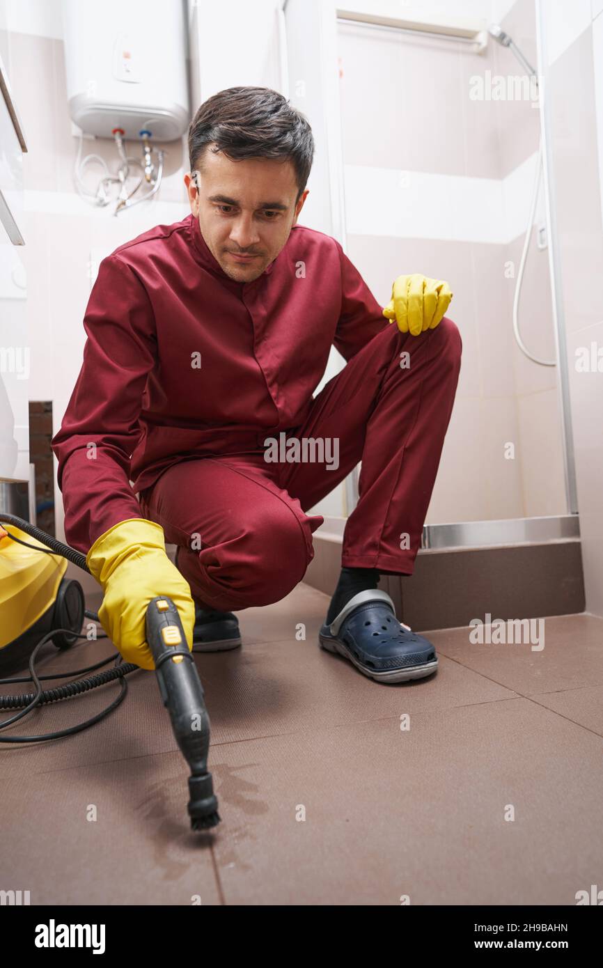 Konzentrierte Dampfreinigungs-Fugenlinie des Hausmeisters auf dem Badezimmerboden Stockfoto