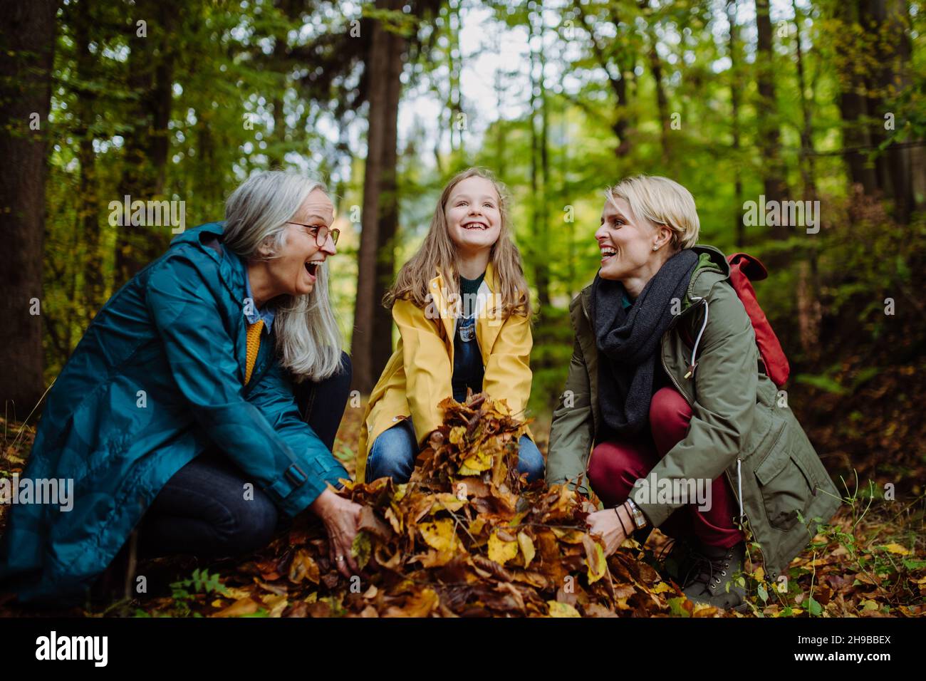 Happy Little girl with mother and Großmutter having fun with blätters during herbsting walk in Stockfoto