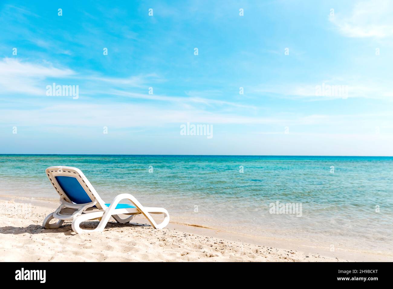 Eine einone Sonnenliege steht direkt am Wasser an der Küste Stockfoto