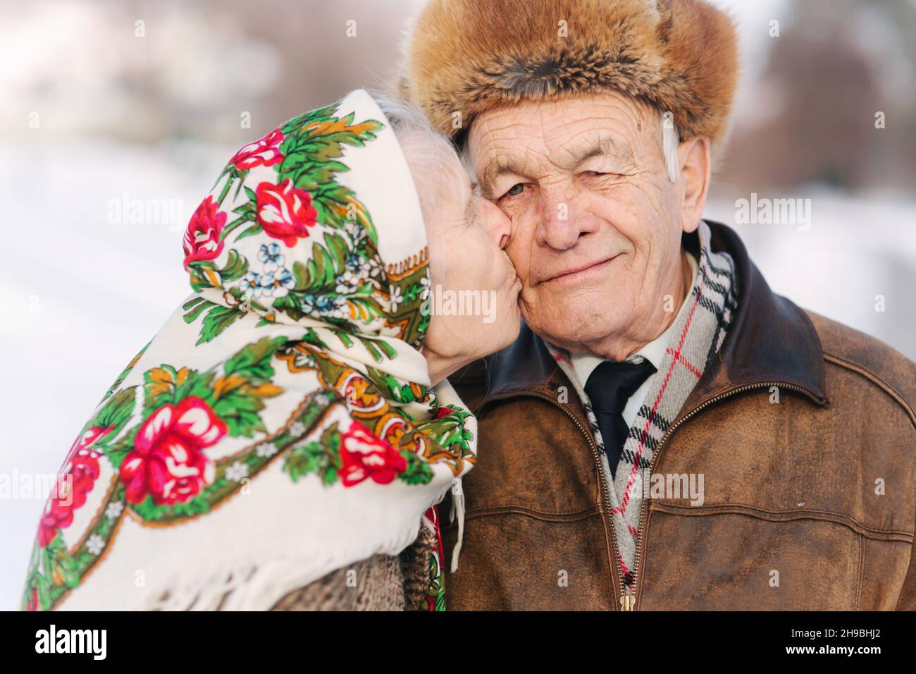 Porträt eines glücklichen älteren Paares. Ältere Frau küssen ihren Mann in gewichtigen. Altes Paar zu Fuß im Park im Winter Zeit. Frohe Familie. Goldene Hochzeit Stockfoto