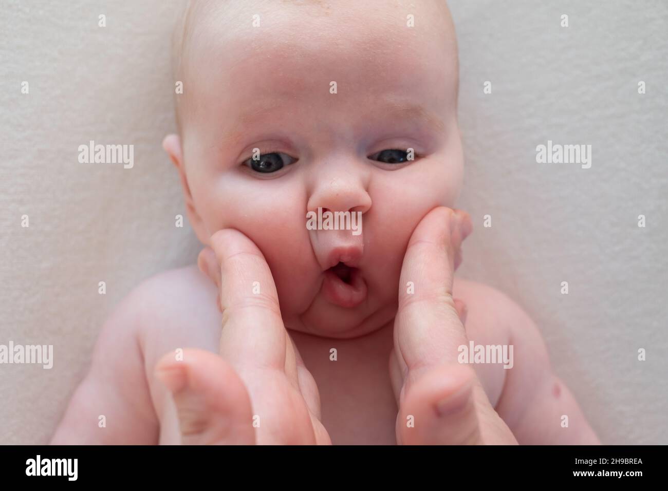 Eltern kneifen Wangen ein kleines neugeborenes Baby Mädchen machen Fisch Gesicht Stockfoto