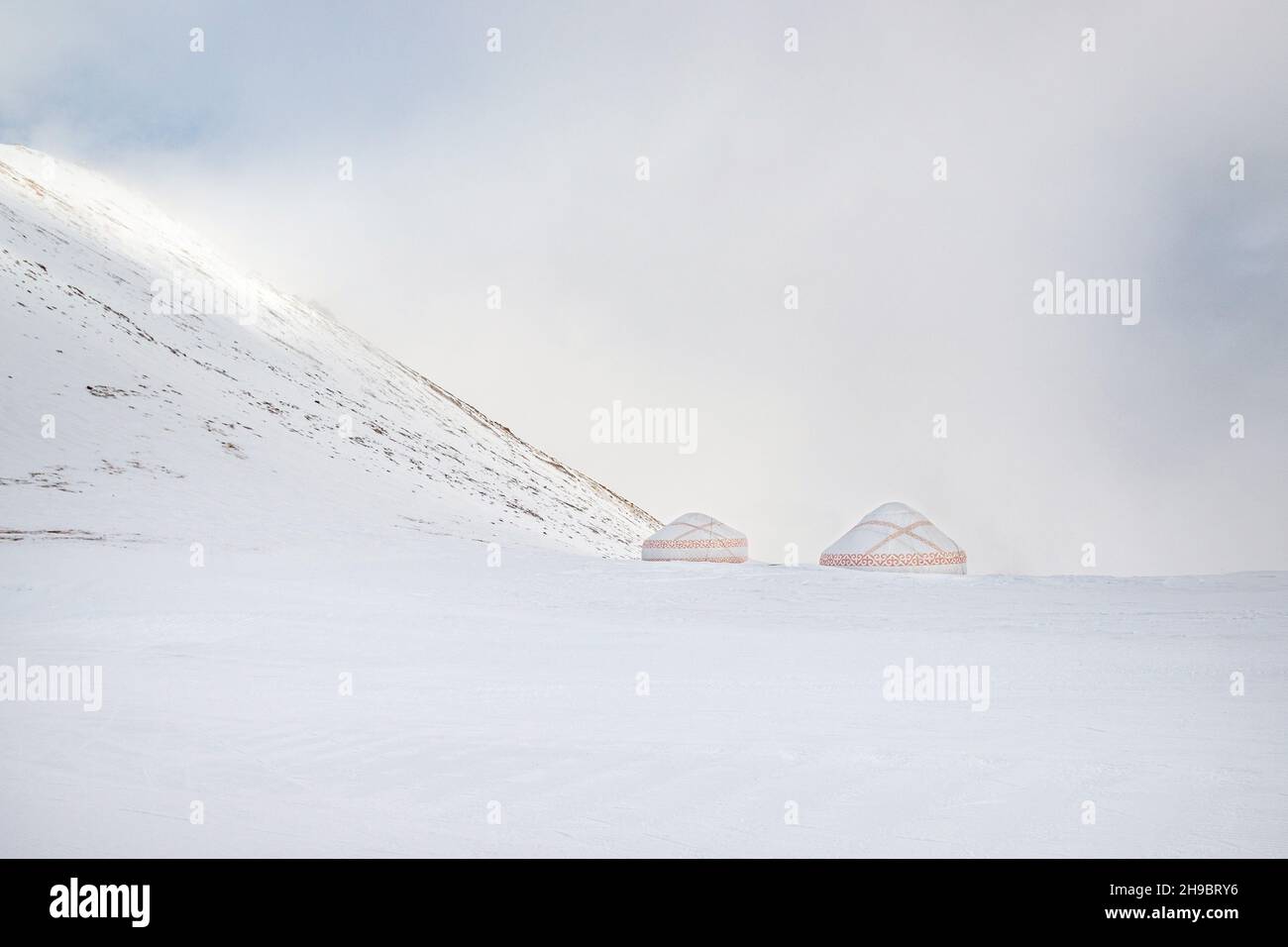 Weiß-rot gemusterte Jurten in einem verschneiten Bergtal. Stockfoto