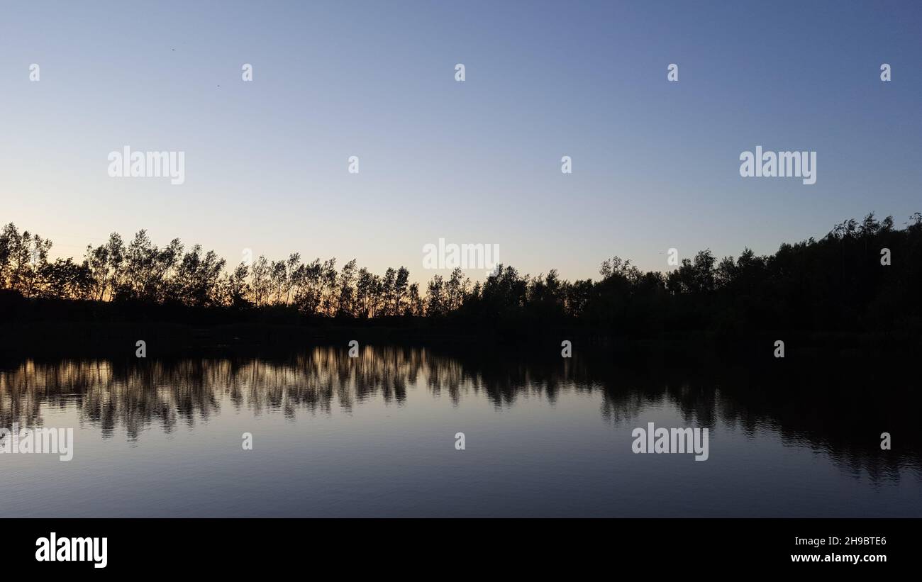 Blick auf einen Teich kurz nach Sonnenuntergang, in einem englischen Park. Reflexionen der Bäume sind im Wasser zu sehen. Stockfoto