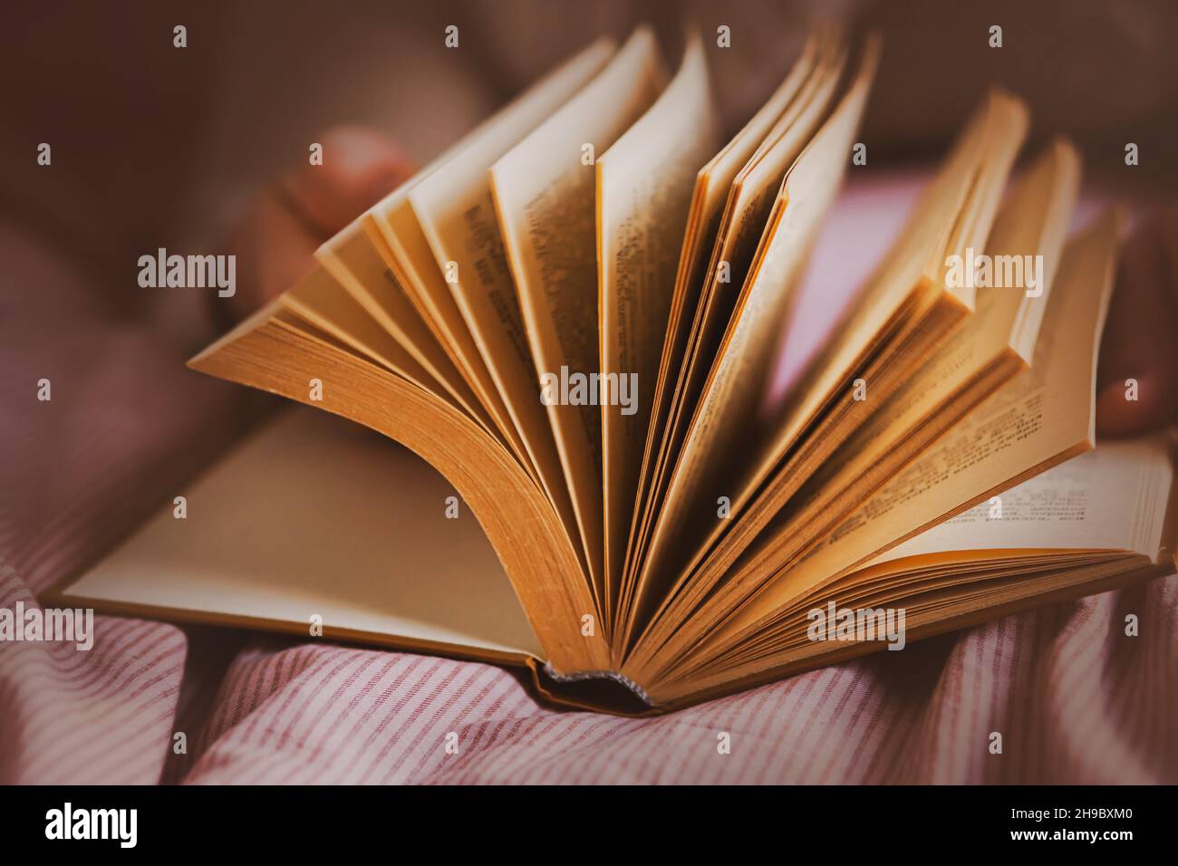 Ein Mann, der auf einem weichen Bett liegt, blättert durch die Seiten eines dicken, interessanten alten Buches. Entspannen beim Lesen eines Romans. Selbstentwicklung. Stockfoto