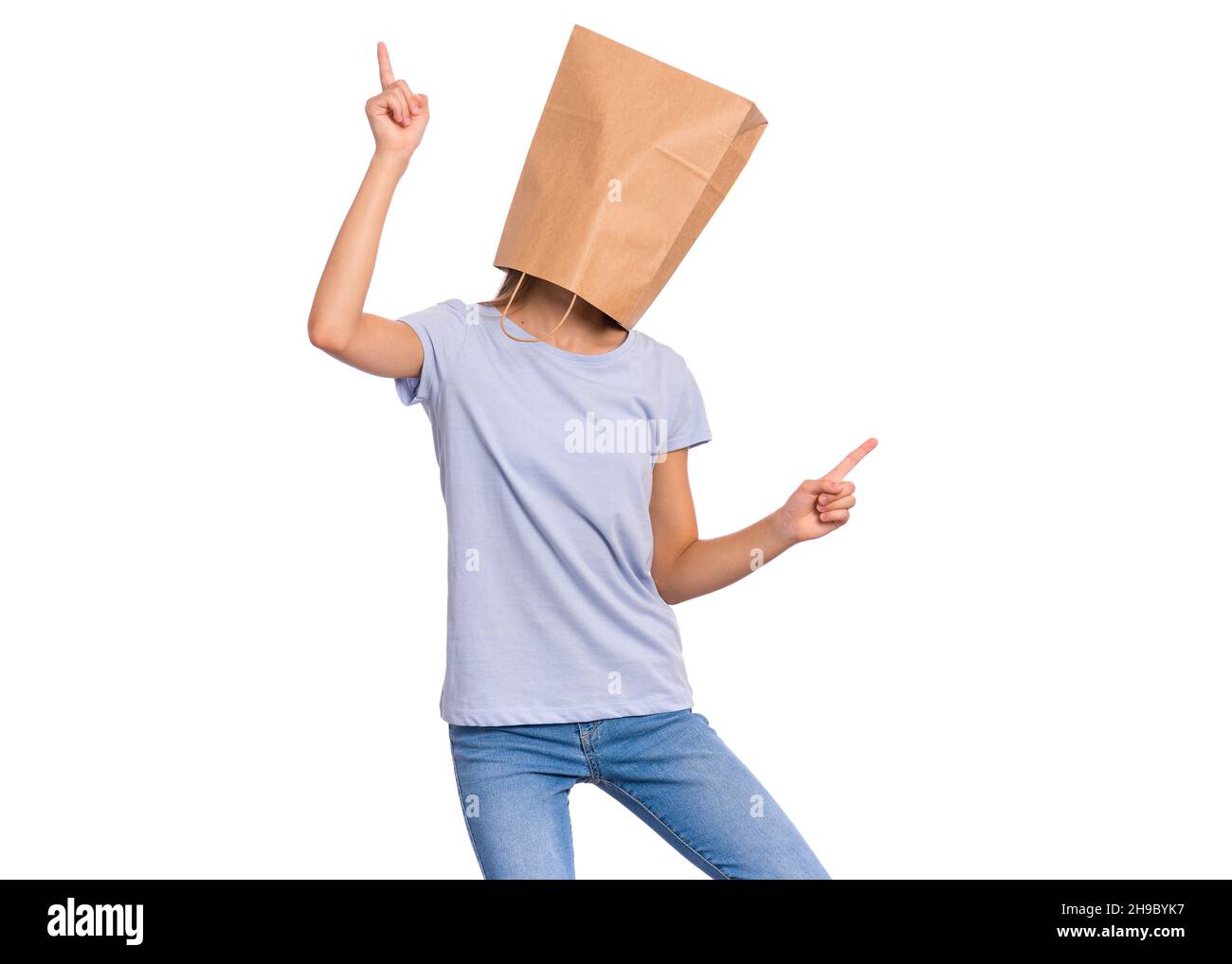 Mädchen mit Papiertüte auf dem Kopf tanzend. Teenager-Cover Gesicht, isoliert auf weißem Hintergrund. Glückliches Kind Zeigen Sie die Finger nach oben. Stockfoto