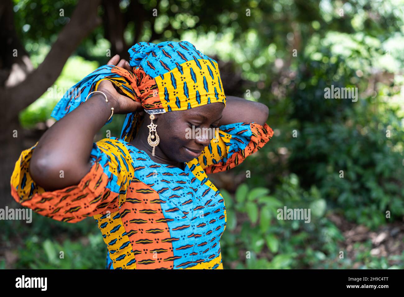 Schöne schwarze afrikanische Frau, die ihren farbigen Schal auf dem Kopf fixiert Stockfoto