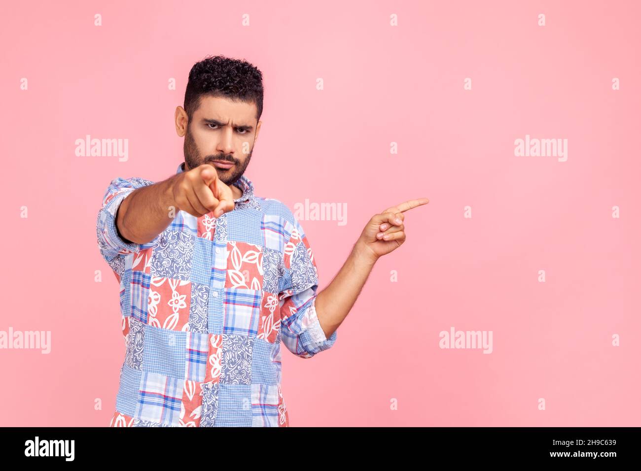 Junge Erwachsene ernsthaft wütend Mann zeigt auf Sie mit dem Finger und präsentiert Bereich mit Förderung, unbedingt darauf achten, hat strengen Ausdruck. Innenaufnahme des Studios isoliert auf rosa Hintergrund. Stockfoto
