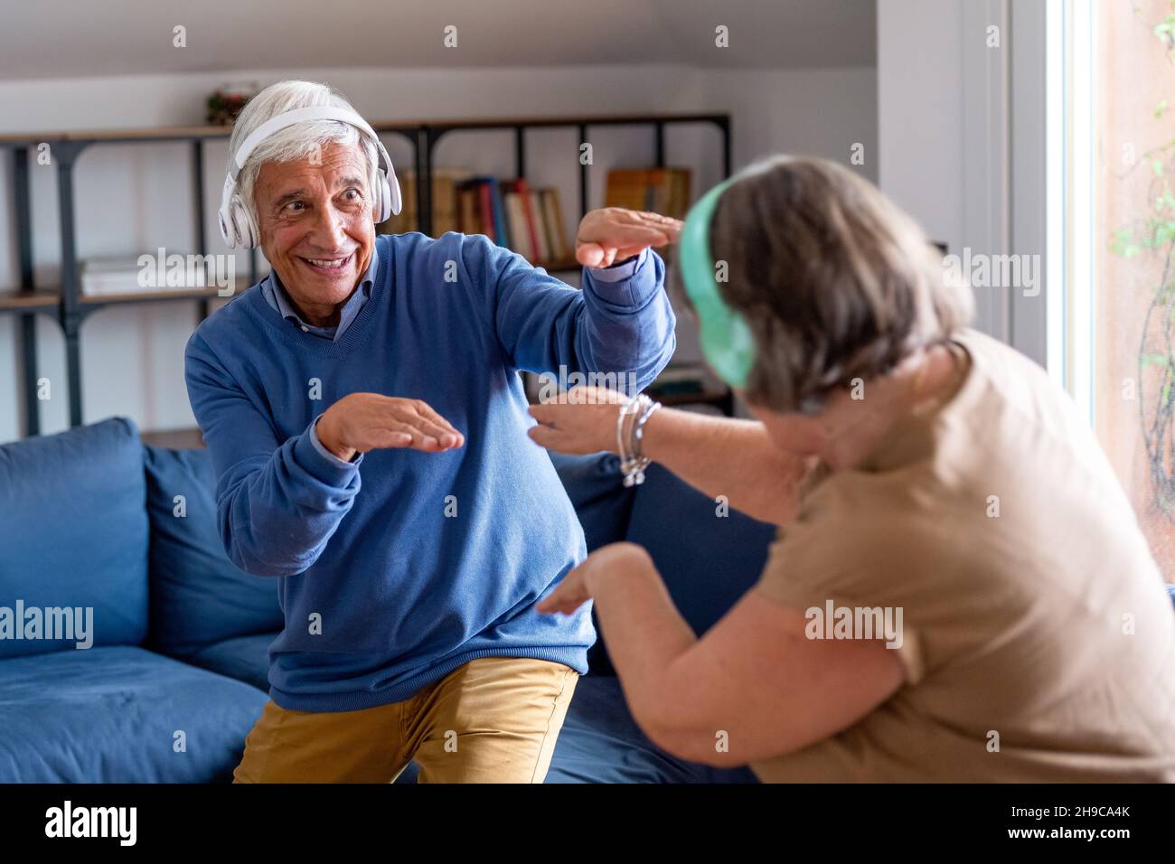 Seniorenpaar zu Hause. Schöner alter Mann und attraktive alte Frau verbringen gerne Zeit zusammen. Spaß haben und tanzen mit kabellosen Kopfhörern Stockfoto
