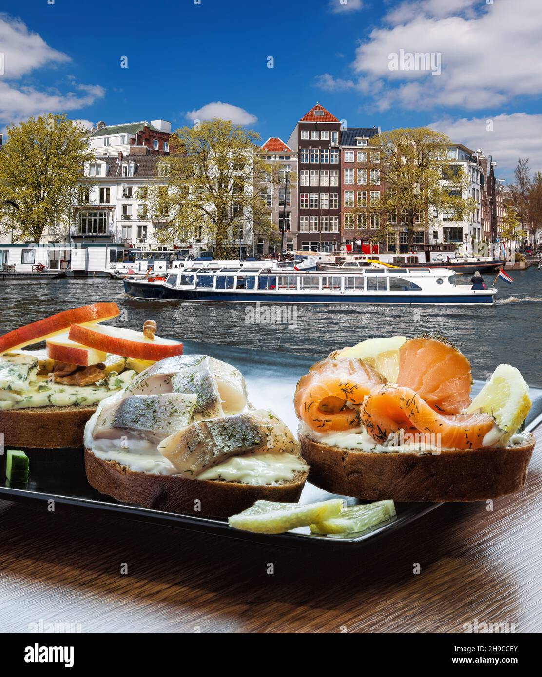 Amsterdam-Stadt mit Fischplatte (salomon- und Kabeljau-Sandwiches) gegen Tourboot auf dem Kanal in den Niederlanden Stockfoto