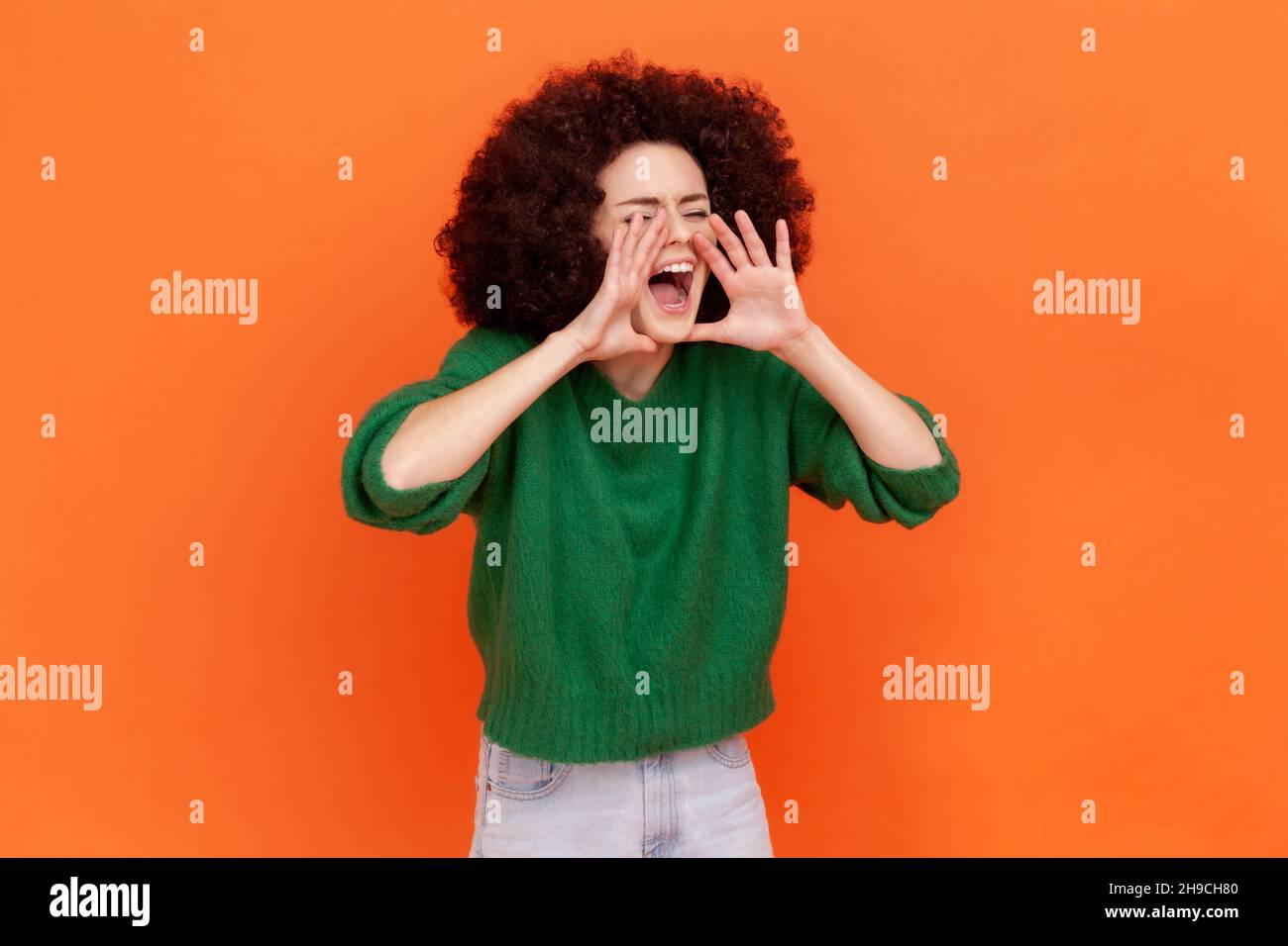 Achtung, Ankündigung. Seitenansicht Porträt einer Frau mit Afro-Frisur trägt grünen lässigen Stil Pullover schreiende Botschaft, laute Werbung. Innenaufnahme des Studios isoliert auf orangefarbenem Hintergrund. Stockfoto