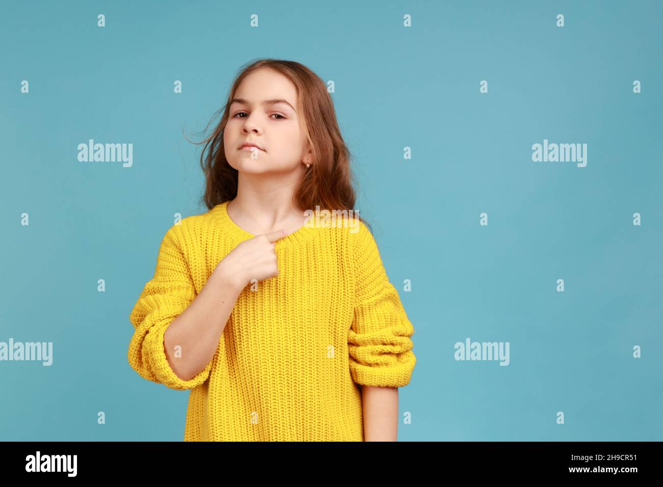 Porträt eines kleinen Mädchens, das stolz auf sich zeigt und sich rühmt, sich berühmt fühlt und einen gelben Pullover im lässigen Stil trägt. Innenaufnahme des Studios isoliert auf blauem Hintergrund. Stockfoto