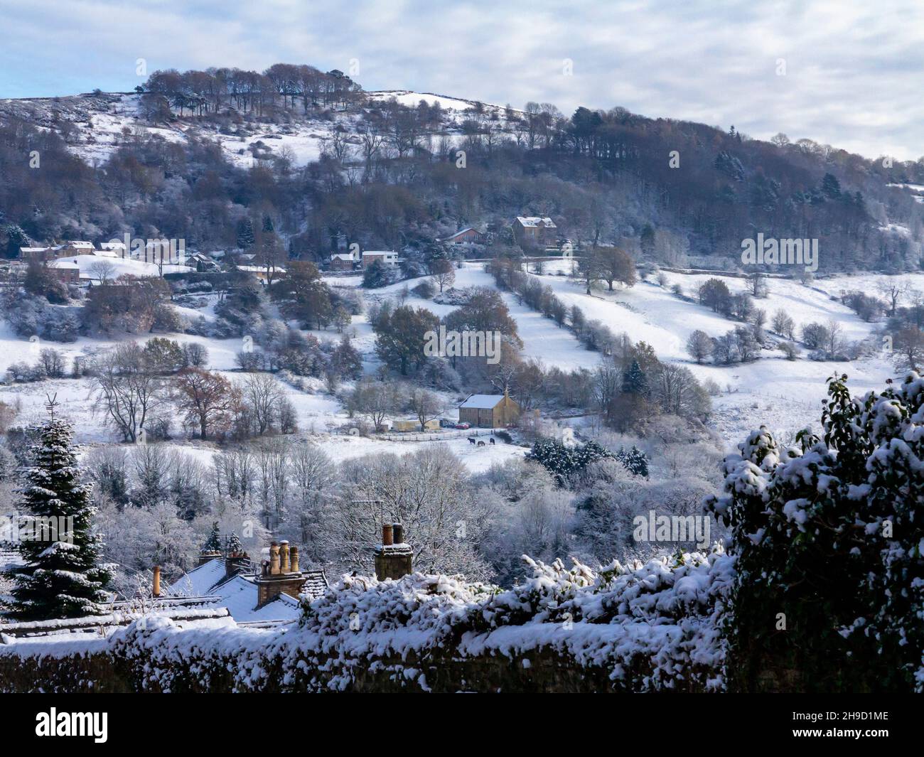 Schneebedeckte Landschaft mit Bäumen in Matlock Bath im Derbyshire Peak District England, Großbritannien, mit dem Dorf Starkholmes, das in der Ferne zu sehen ist. Stockfoto