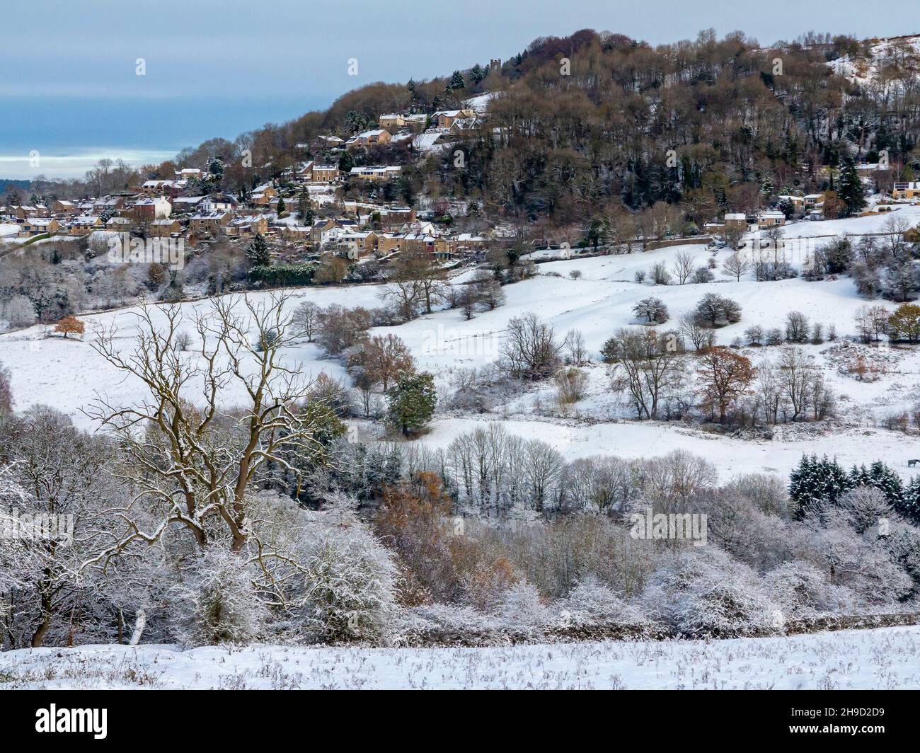 Schneebedeckte Landschaft mit Bäumen in Matlock Bath im Derbyshire Peak District England, Großbritannien, mit dem Dorf Starkholmes, das in der Ferne zu sehen ist. Stockfoto