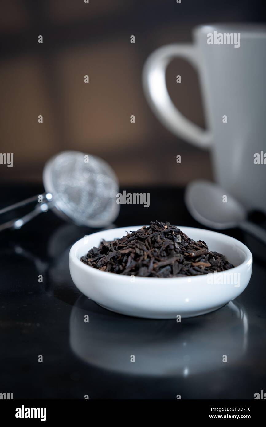 Helsinki / Finnland - 4. DEZEMBER 2021: Selektive Nahaufnahme einer Tasse mit frischen Teeblättern. Ein unfokussieren Teesieb im Hintergrund. Stockfoto