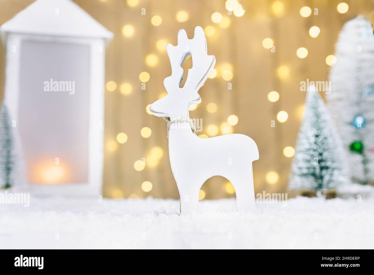 Weihnachtsmärchen Komposition mit weißem Holzwild Spielzeug, Laterne und kleinen Weihnachtsbäumen auf dem Schnee vor warmen Lichtern Bokeh Hintergrund. Frohe Stockfoto