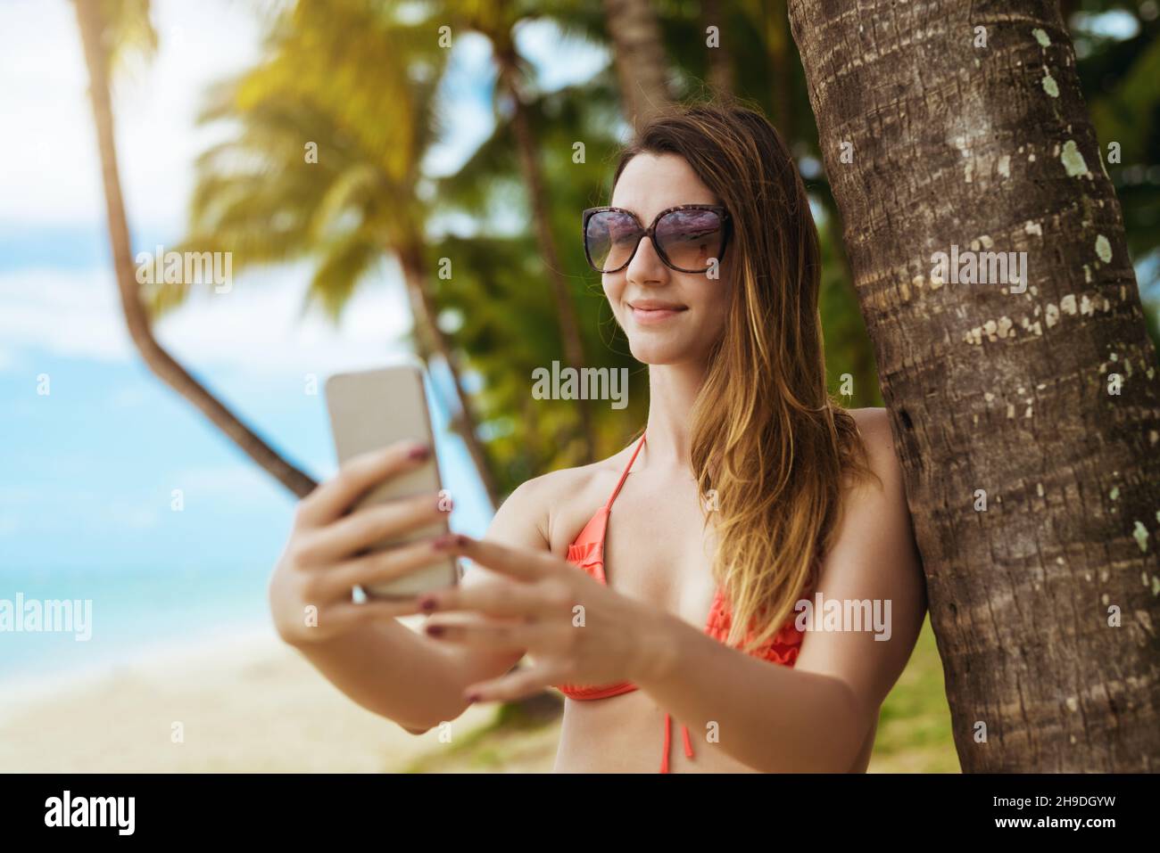 Schöne Frau in Mode Bikini nimmt Selfie auf schönen tropischen Hintergrund. Videoanruf mit Freunden Stockfoto