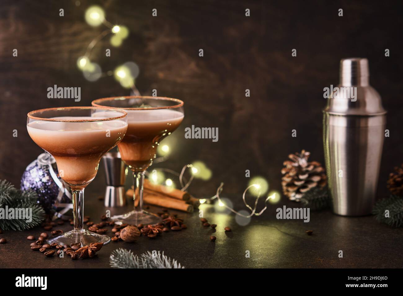 Alexander Cocktail in Cocktailglas auf Holztisch mit Shaker, Muskatnuss und kleiner Reibe mit weihnachtlicher Dekoration auf dunklem Hintergrund. Getränkefoto Stockfoto