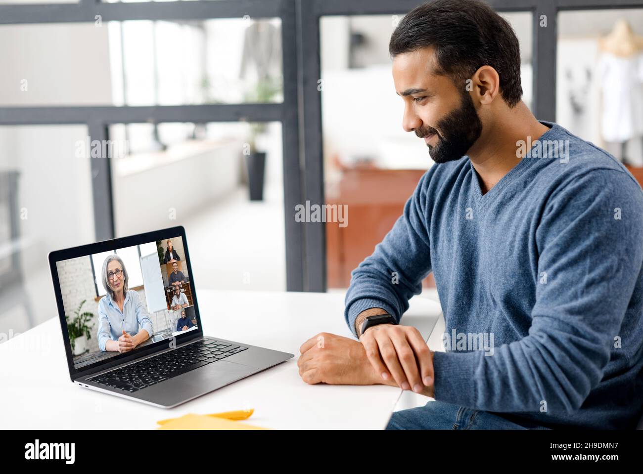 Indischer Student, der online studiert, ein Webinar mit einer Lehrerin ansieht und andere Studenten daran beteiligt ist. Ethnischer, multirassischer Mann, Mitglied einer Videokonferenz, der einen Laptop für die Online-Verbindung verwendet Stockfoto