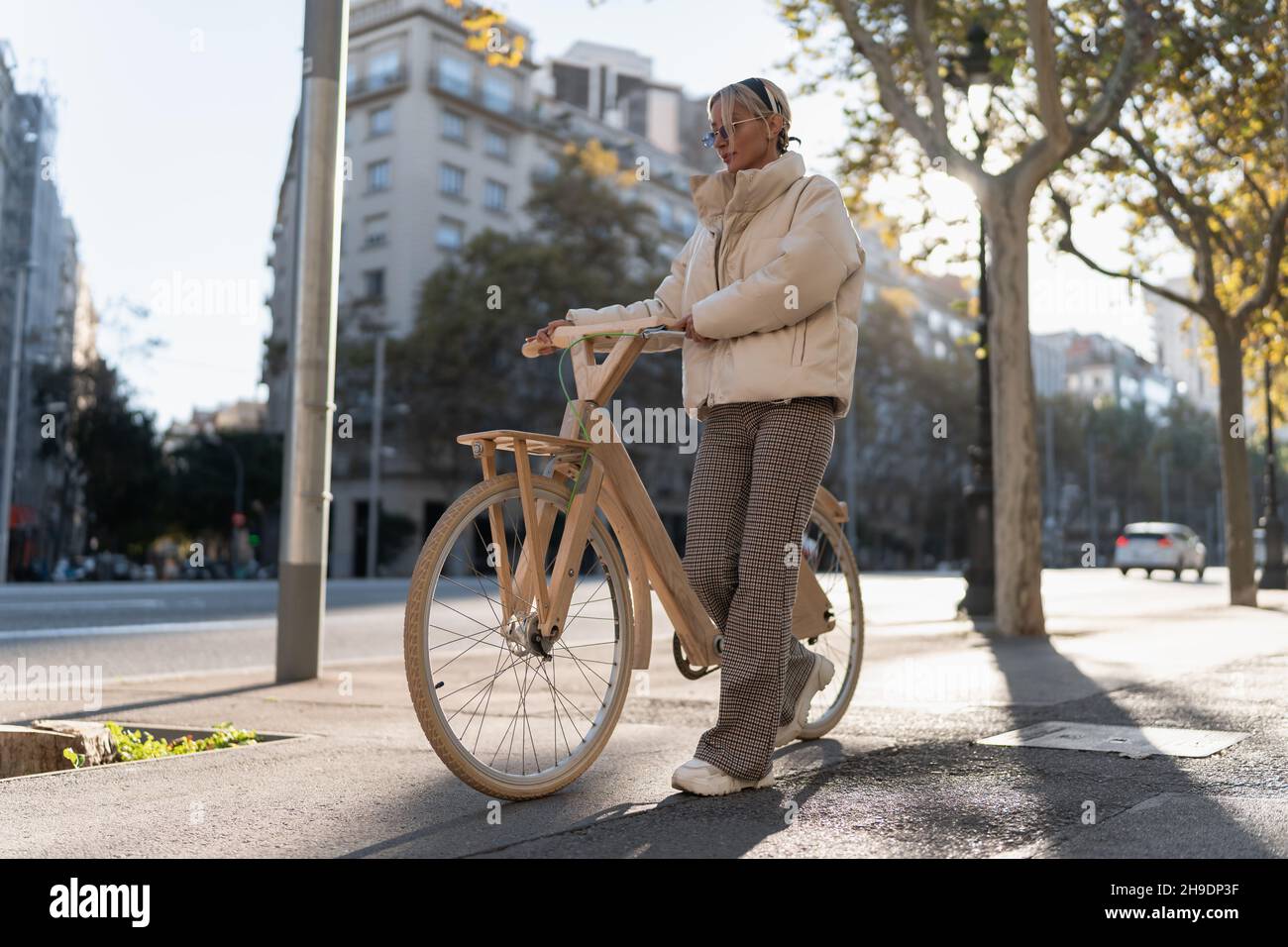 Ganzkörper trendige weibliche Schieben Holz Öko Fahrrad während zu Fuß in der Nähe der Straße an sonnigen Tag in der modernen Stadt. Stockfoto