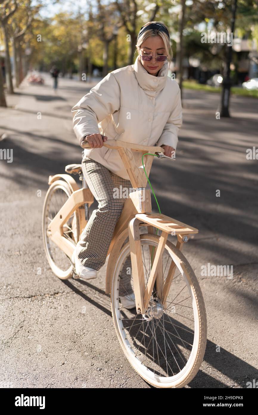 Ganzkörper Erwachsene Frau beginnt, Holz Öko-Fahrrad auf Asphaltweg am sonnigen Herbsttag im Park zu fahren. Stockfoto