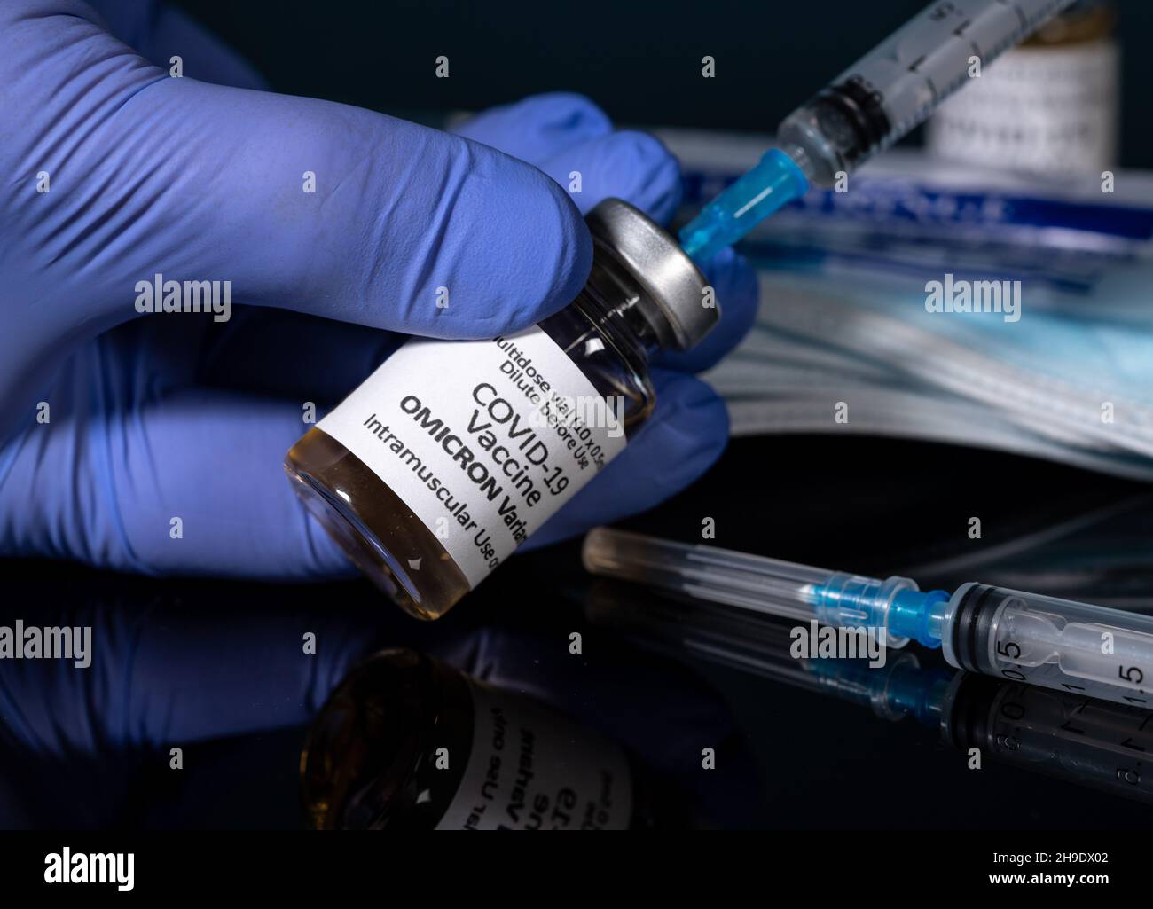 Covid-19-Coronavirus-Impfstoff entwickelt für Omicron-Variante, mit Handschuhen gehalten, mit hypodermischer Spritzennadel und neuen Spritzen im Hintergrund Stockfoto