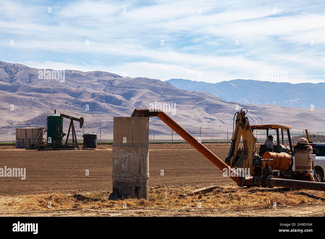 Landwirt im Traktor neben Brachfeld und Ölbrunnen, Arvin, Kern County, Kalifornien, USA Stockfoto