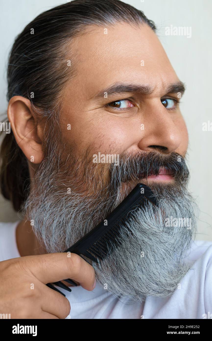 Nahaufnahme eines kaukasischen Mannes mittleren Alters mit Haarbürste. Er kämmt seinen grauen Bart. Selektiver Fokus. Stockfoto
