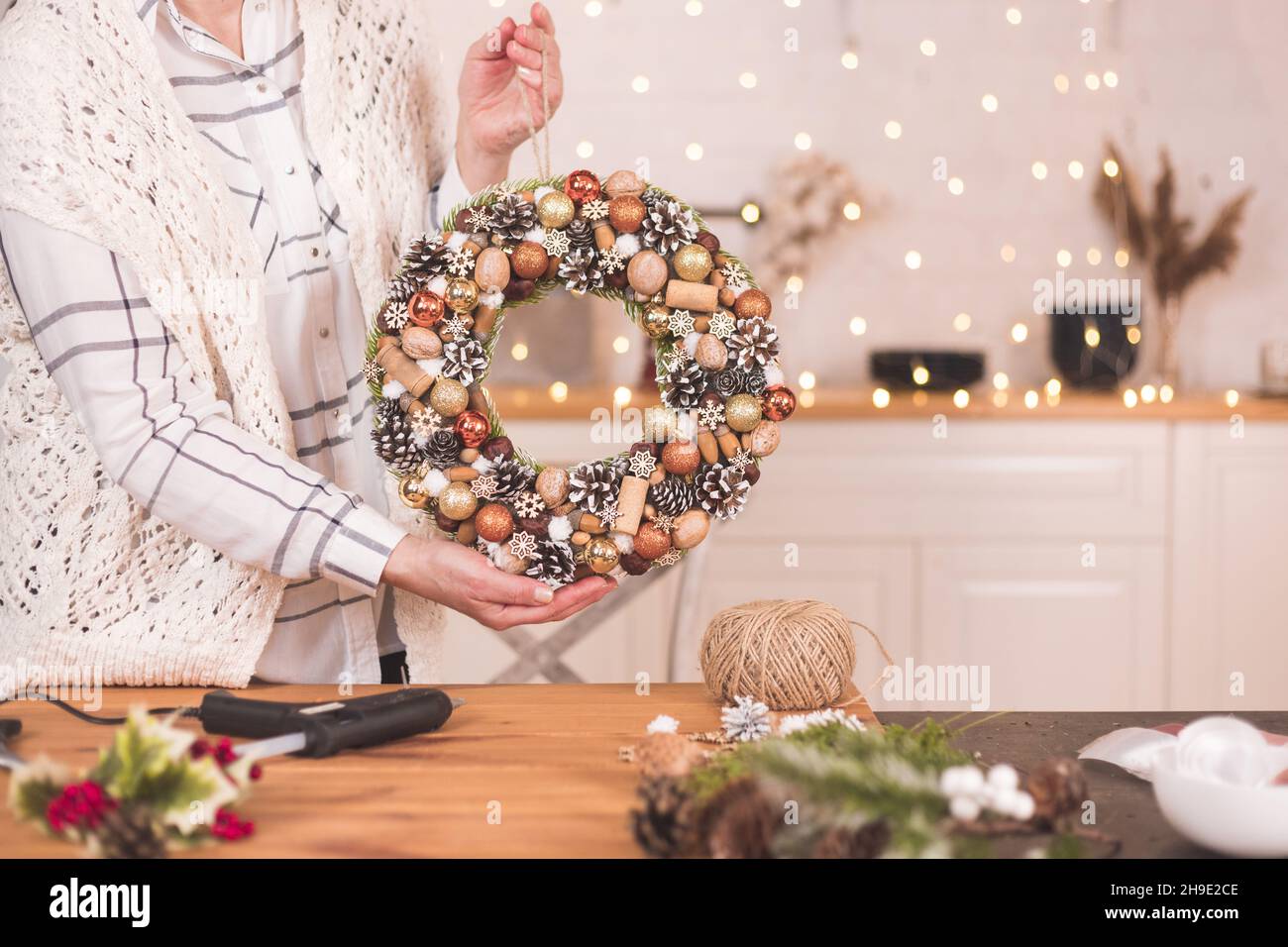 Frau mit modernem rustikalem weihnachtskranz. Rustikaler weihnachtskranz in weiblichen Händen mit Tannenzweigen, Beeren und Kegel Stockfoto