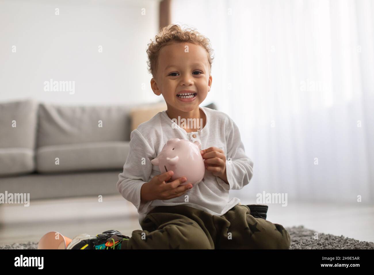 African American Little Boy Holding Sparschwein Mit Persönlichen Ersparnissen In Der Halle Stockfoto