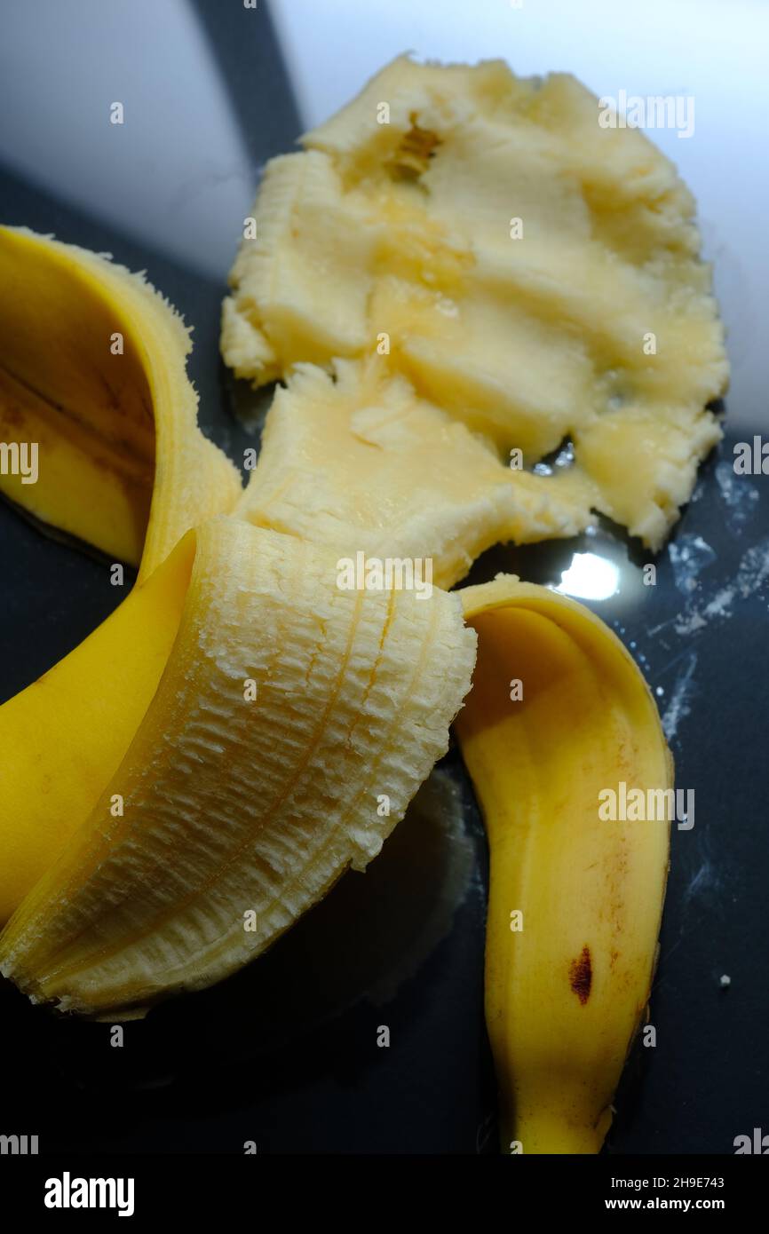 Zertrümmerte einfarbige reife gelbe Banane auf dunklem reflektierendem Hintergrund Stockfoto