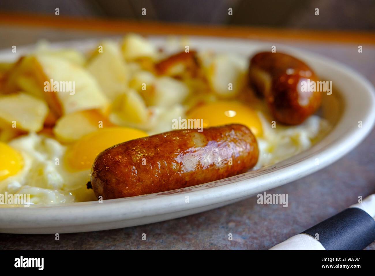 Komplettes amerikanisches Diner-Frühstück, drei sonnige Spiegeleier, Würstchen und Pommes frites Stockfoto