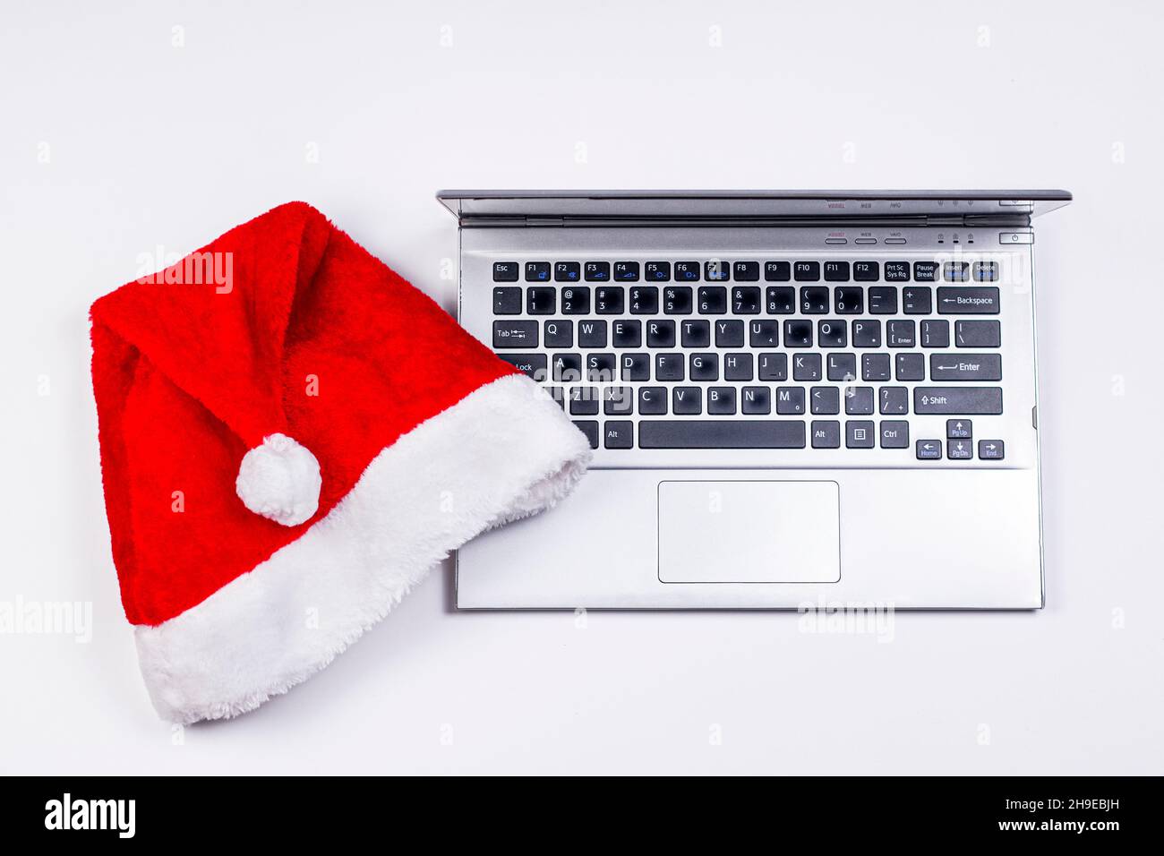 Weihnachtsmannhut und alter Laptop auf weißem Hintergrund. Weihnachtsurlaub und Neujahrsurlaub Konzept. Stockfoto