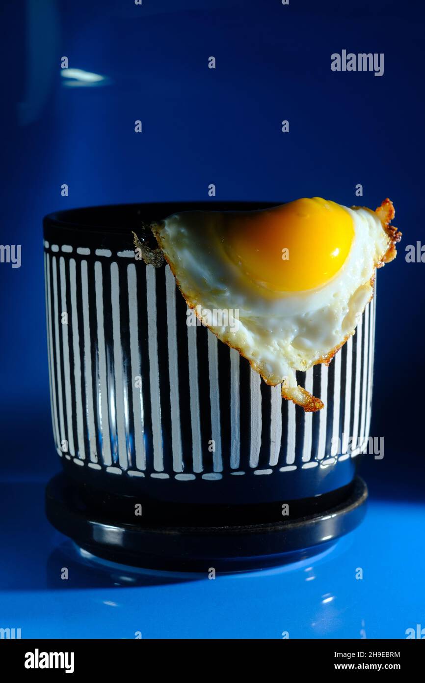 Abstraktes, gebratenes, sonniges Eierfrühstück, serviert in gestreiftem Pflanzentopf als Metapher für Wachstum und Entwicklung Stockfoto