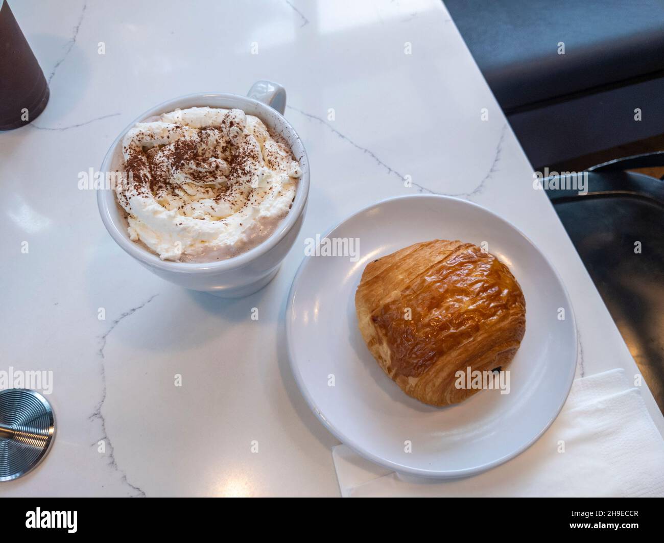 Blick von oben auf einen Kaffee mit Schlagsahne und einem Pain au Chocolat auf einem weißen Marmortisch. Stockfoto