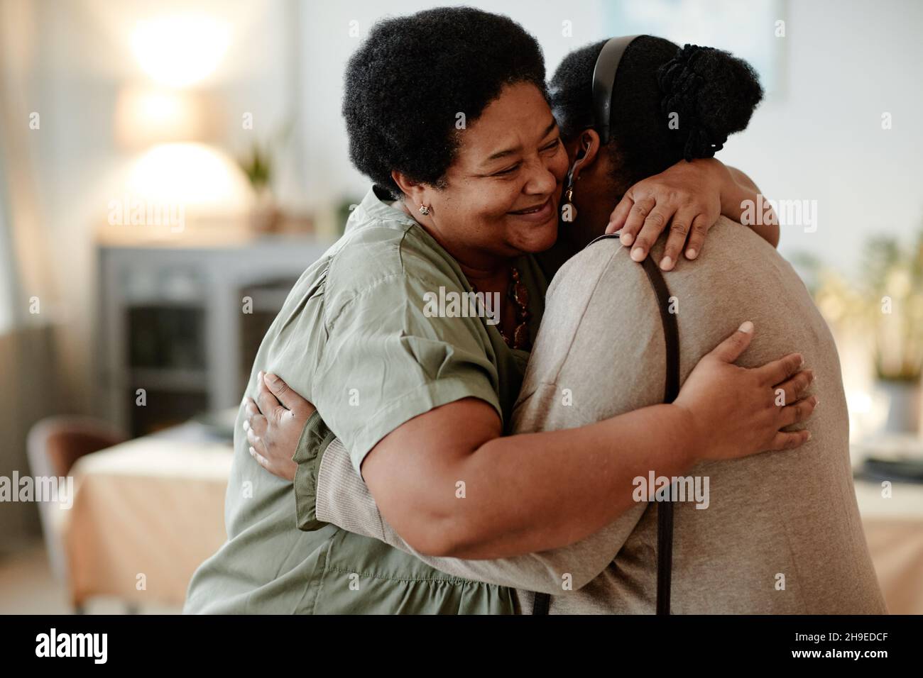 Porträt einer älteren afroamerikanischen Frau, die ihre Tochter umarmt und lächelt, während sie die Gäste zu einer Dinner-Party zu Hause begrüßt Stockfoto