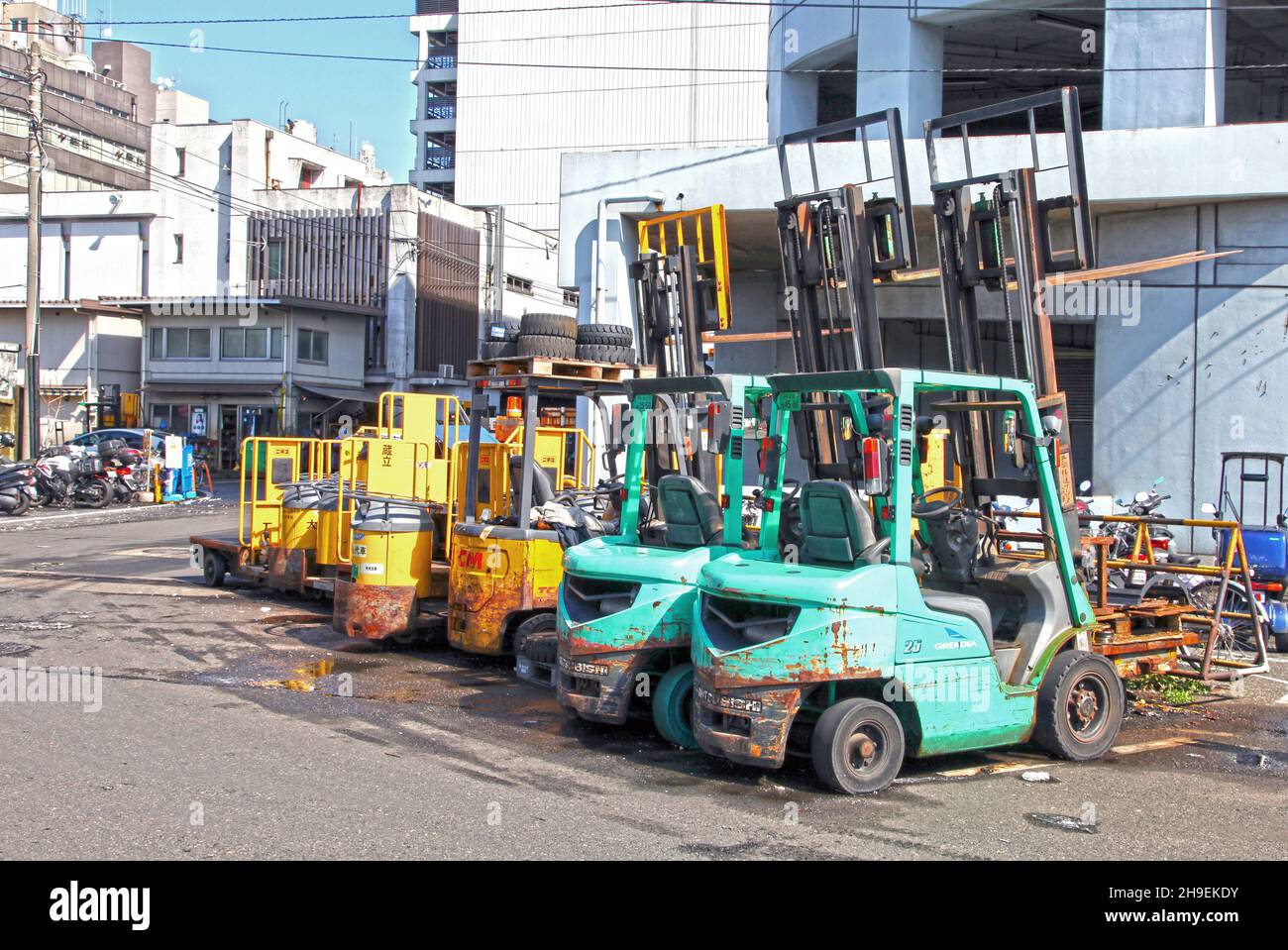 Kleine Gabelstapler in Türkis und Gelb, die vor einem Lagerhaus neben dem Tsukiji Fischmarkt in Tokio, Japan, geparkt sind. Stockfoto