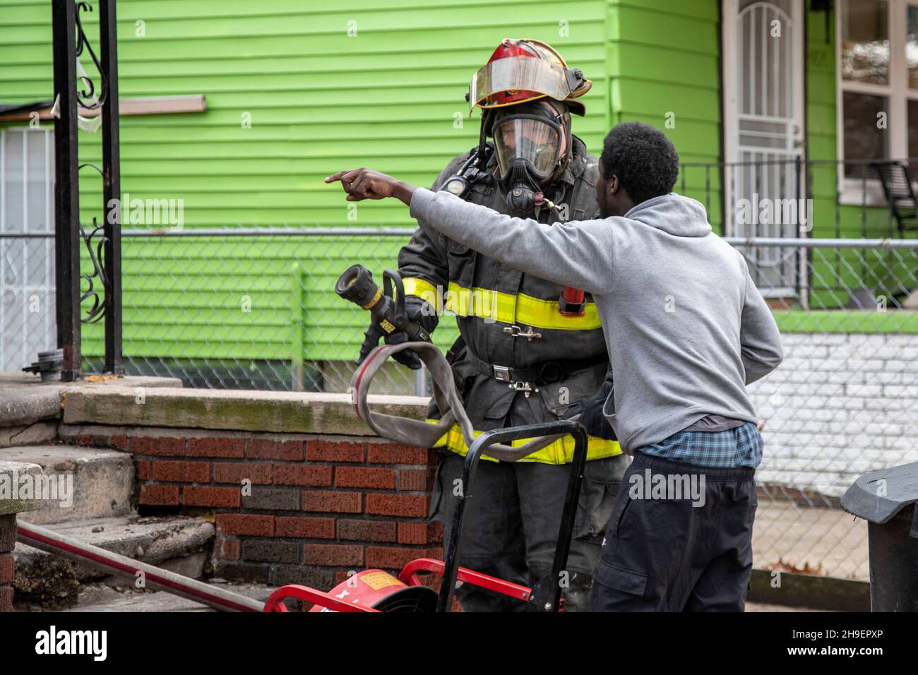 Detroit, Michigan - Ein Bewohner eines brennenden Hauses zeigt in das Gebäude, während er mit einem Feuerwehrmann spricht, der am Tatort ankommt. Das Feuer beschädigte ein Haus Stockfoto
