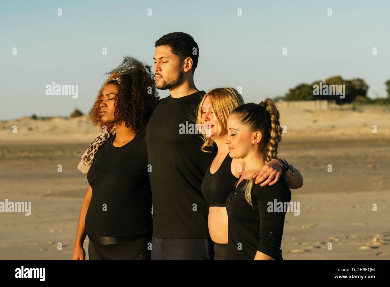 Multiethnische Yogastunde, die sich für die Schultern umarmen, während sie sich am Strand entspannen Stockfoto