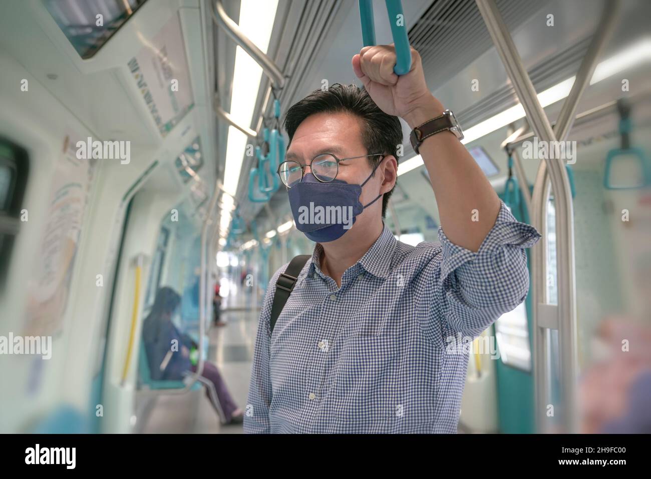 Asiatischer Mann Pendler mit Gesichtsmaske auf halten an Hand Griff in einem beweglichen Zug. Maskiertes Transitkonzept. Stockfoto
